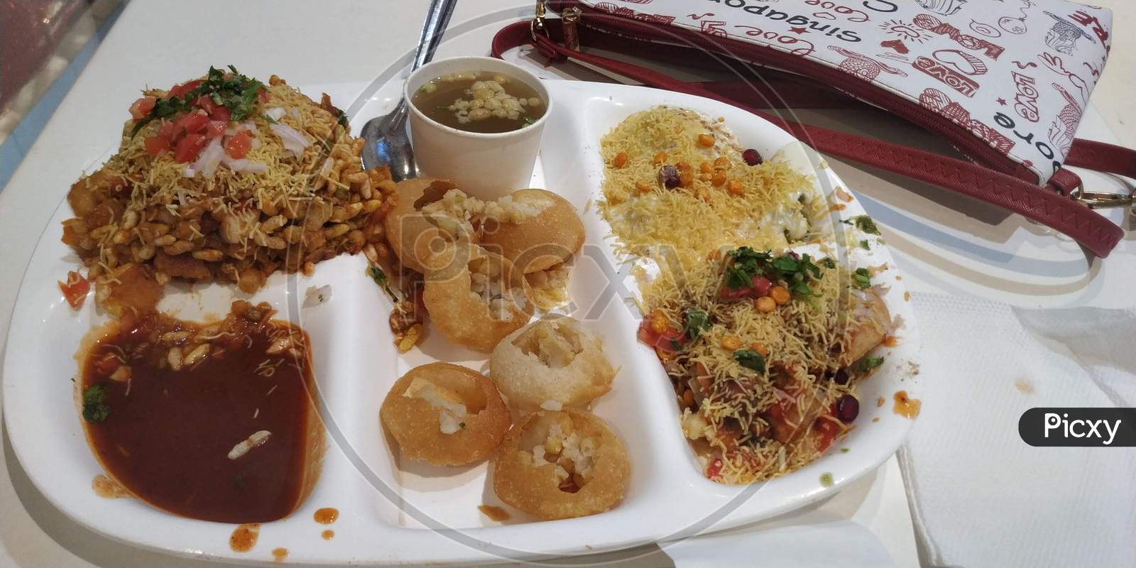 Famous Indian Street Food With Bhel , Panipuri And Papdi Chat With Sweet And Spicy Chutney With Onion And Aloo Or Potato Masala On White Plate