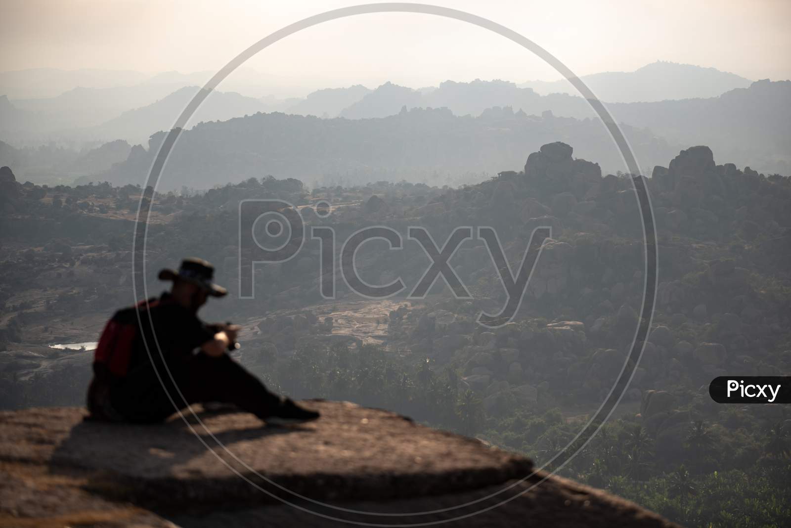 A Foreigner with Camera Sitting On The Edge Of A Rock In The Mountains.