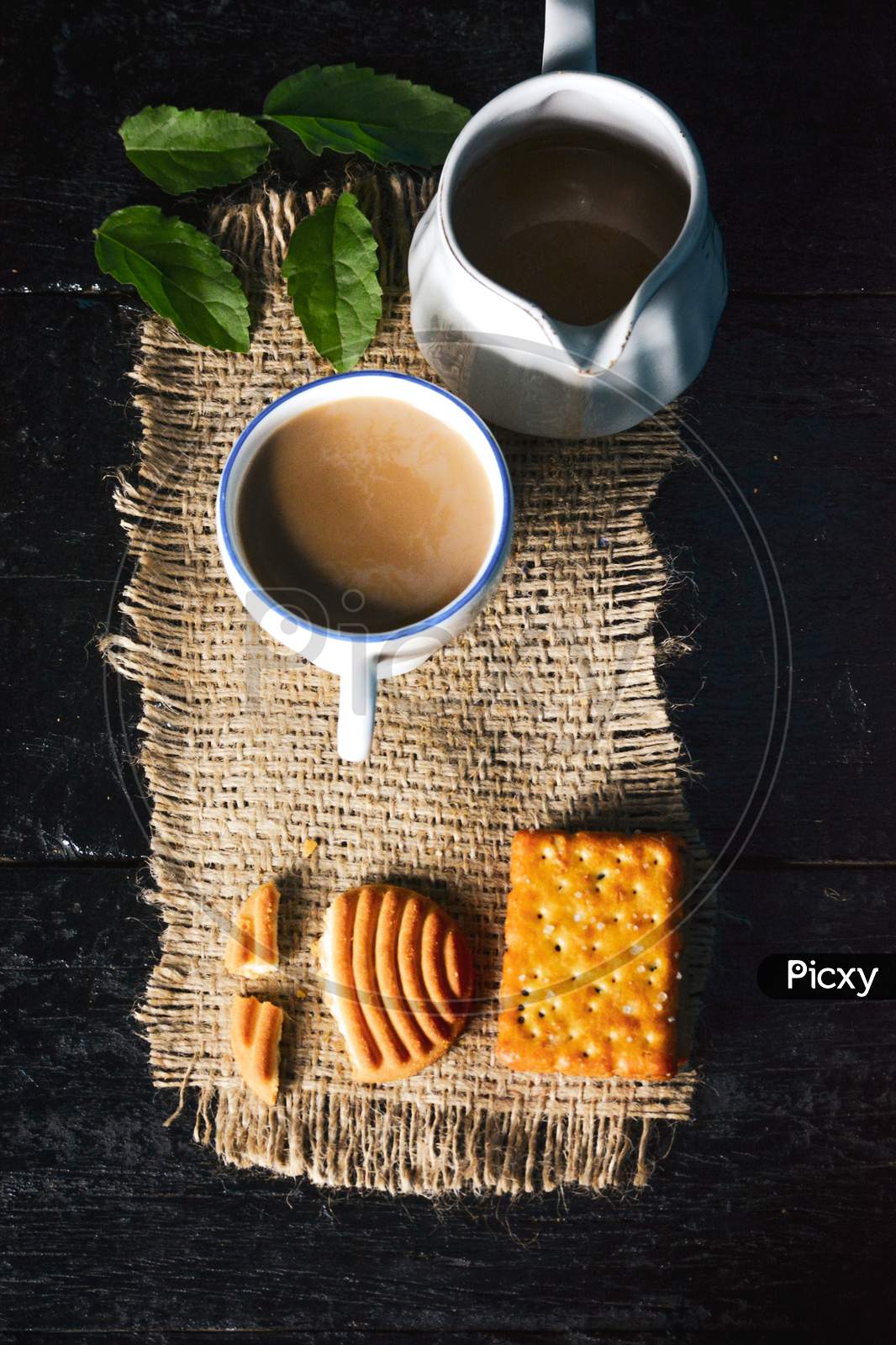 A cup of tea with tasty biscuits, teapot and fresh Leaves on old wooden dark background