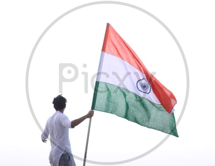 Cheerful young Indian man standing and holding national flag for motivation on top of roof during lock down