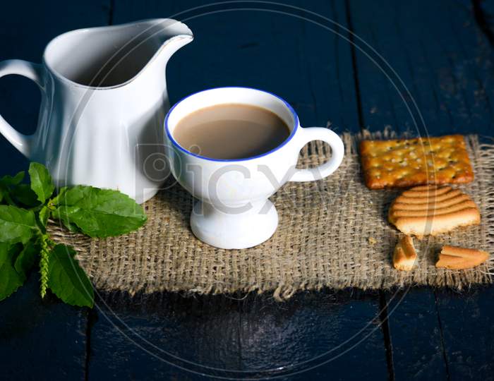 A cup of tea with tasty biscuits, teapot and fresh Leaves on old wooden dark background