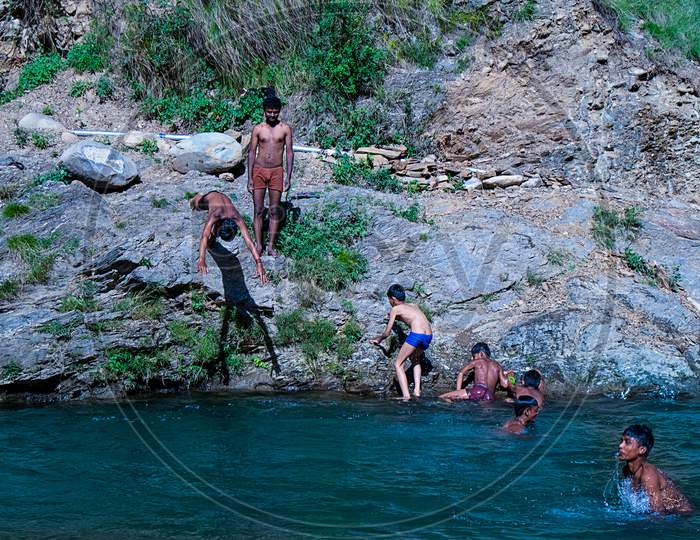 Nehrwa, Himachal Pradesh, India - April 20Th, 2019: Playful Children Swimming In Fresh River Water On A Summer Vacations Surrounded By Beautiful Green Hill Mountains