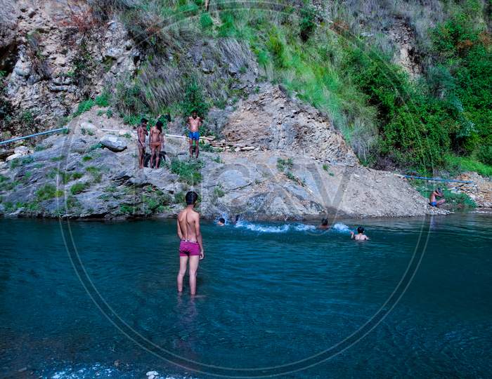 Himachal Pradesh, India - April 20Th, 2019: Playful Children Swimming In Fresh River Water On A Summer Vacations Surrounded By Beautiful Green Hill Mountains