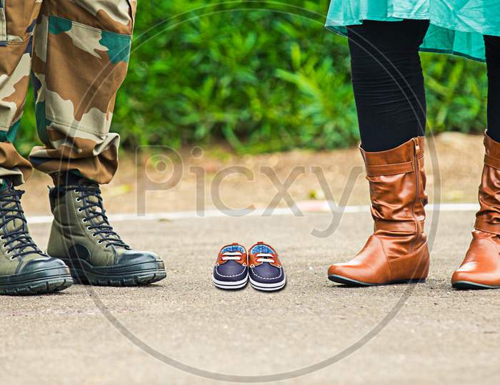 Close Up Of Man Army Shoes And Woman In Brown Leather Boots Along With Little Baby Shoes, Family Maternity Concept.