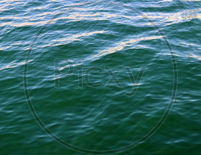 Detailed close up view on water surfaces with wave and ripples and the sunlight reflecting at the surface