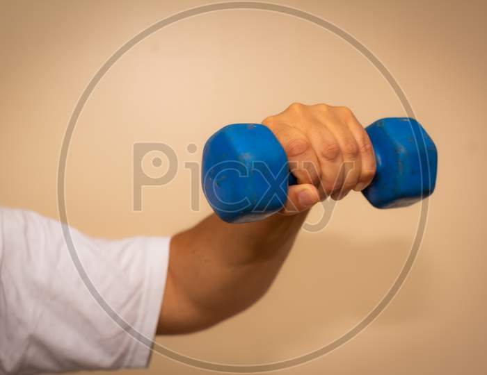 Adult Man Doing Exercise In The Gym. Man With Small Blue Weights. Health And Wellness Concept.