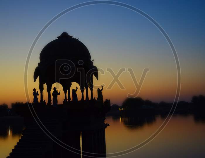 Silhouette Of Temple On The Gadi Sagar Lake With Four People Standing Sunset Sky In Jaisalmer, Rajasthan, India