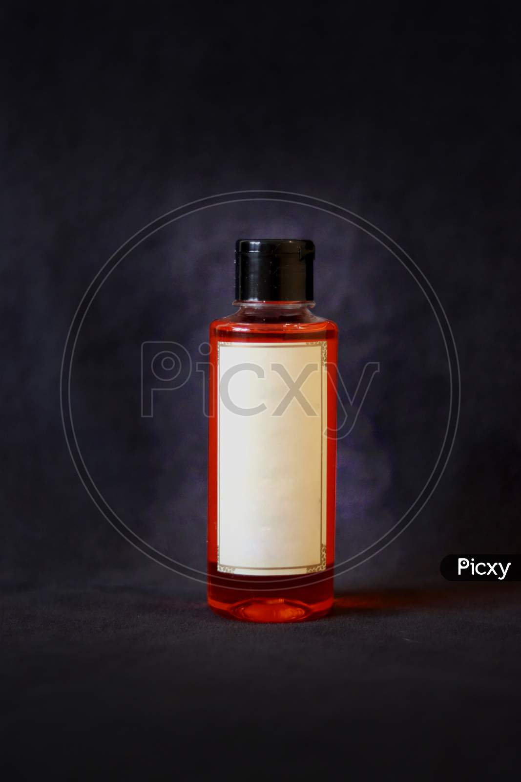Orange Oil Bottle With Off White Label And Black Bottle Cap On Dark Grey Textured Background.