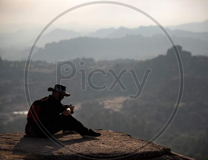 A Foreigner with Camera Sitting On The Edge Of A Rock In The Mountains.