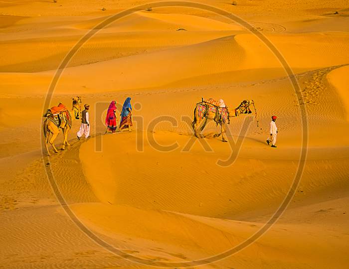 Jaisalmer, Rajasthan, India - April 18Th, 2018: Cameleers With Camels Walking On Golden Sand Dunes Of Thar Desert, Jaisalmer, Rajasthan, India