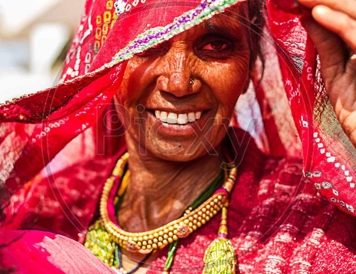 Jodhpur, Rajasthan, India - May 18Th, 2019 : Wrinkled Old Village Woman In Veil Wearing Red Saree And Gold Necklace Smiling, Concept Of Hope And Dreams