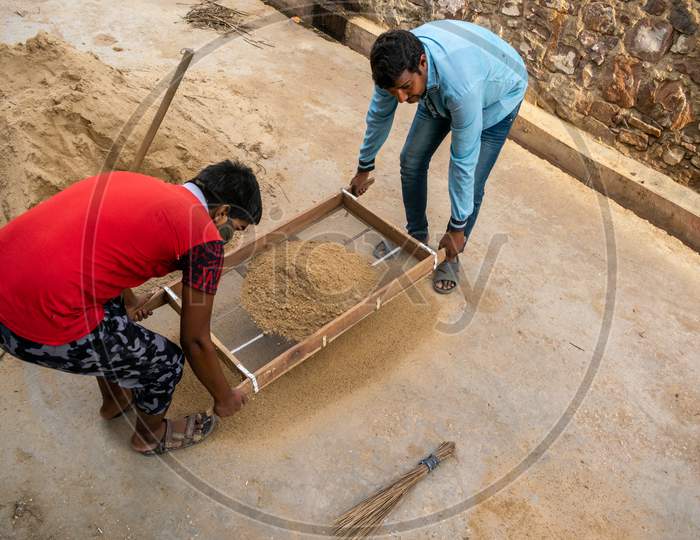 A man and a boy sieve bajri or gravel using sieve for construction purpose for their house
