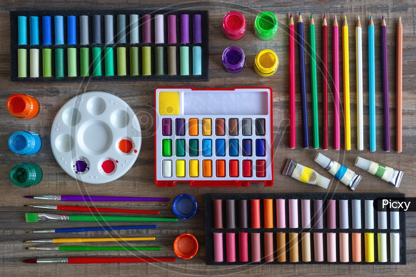 Colorful stationery flat lay: pastel crayons, colored pencils, watercolors on wooden background. Art workspace school concept. Top view