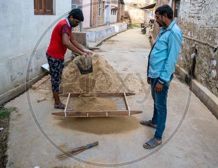 A man and a boy put bajri or gravel in a sieve to sieve it for construction