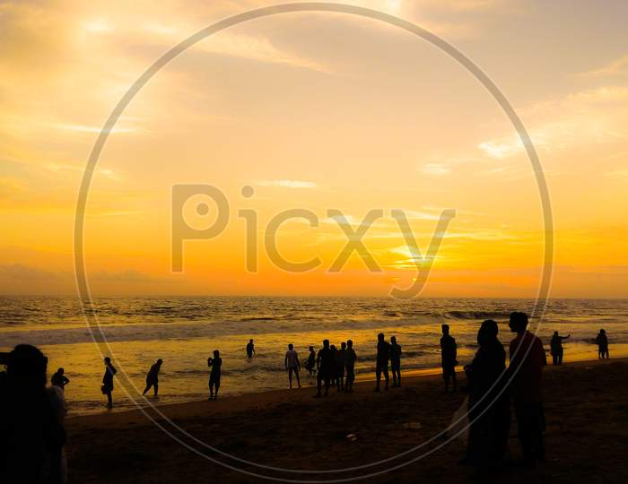 A Silhouette Landscape Image Of People Watching Sunset On A Beach In Kerala, India.