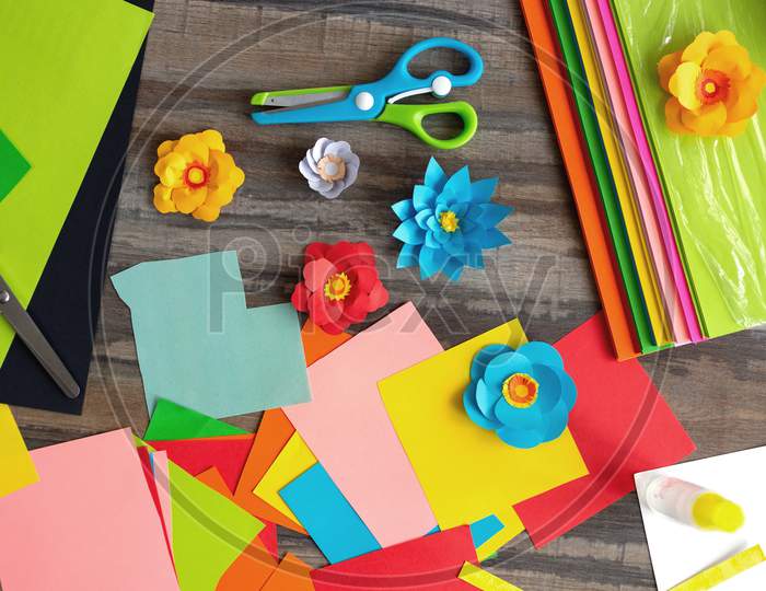 Flat lay of colorful  color paper flowers and scissors on wooden desk. Art studio workplace concept