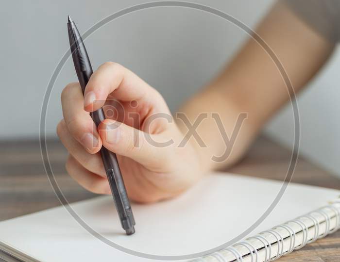 Vintage close up of female hand writing taking notes with pen in blank spiral notebook.