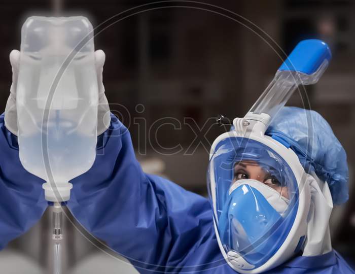 This Is Photograph Of Ppe Kit Wearing Doctor In Covid Hospital Have Shallow Depth Of Field Selective Focus Blur And Wonderland Background In Newyork Usa Hospital Holding Glucose Bottle During This Epidemic Pandemic Of Corona Virus.