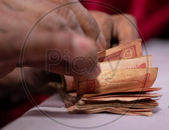 A man counting Indian currency notes of twenty 20 rupees put on table