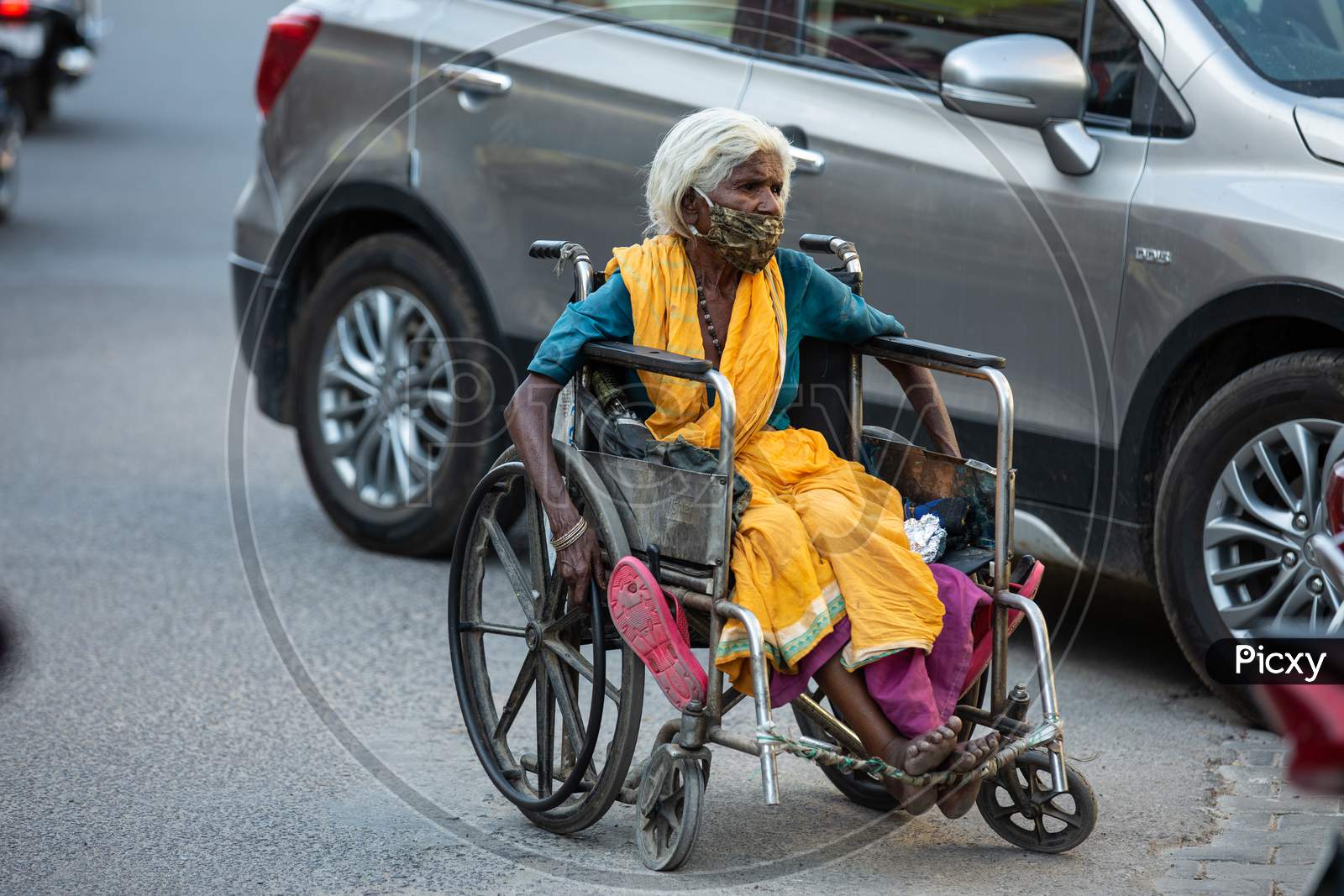 Jodhpur, Rajasthan, India - May 20 2020: Poor Helpless Handicapped Old Woman Sitting In Wheelchair Wearing Mask Roaming On Road During Covid-19 Lockdown Crisis, No Food To Eat No Place To Go.