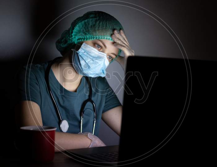 Caucasian woman doctor nurse in surgical mask looks tired, exhausted at night because of covid