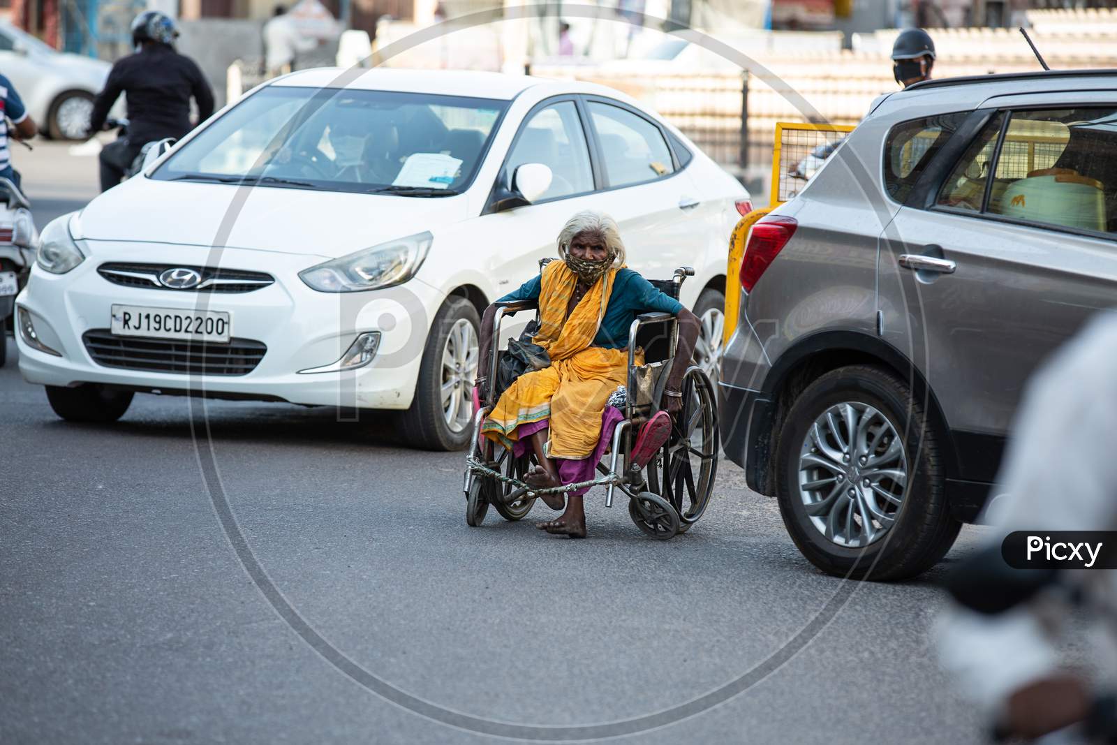Jodhpur, Rajasthan, India - May 20 2020: Poor Helpless Handicapped Old Woman Sitting In Wheelchair Wearing Mask Roaming On Road During Covid-19 Lockdown Crisis, No Food To Eat No Place To Go.