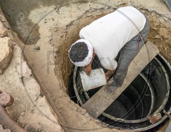 A man pouring concrete in a mould to construct septic tank outside a house