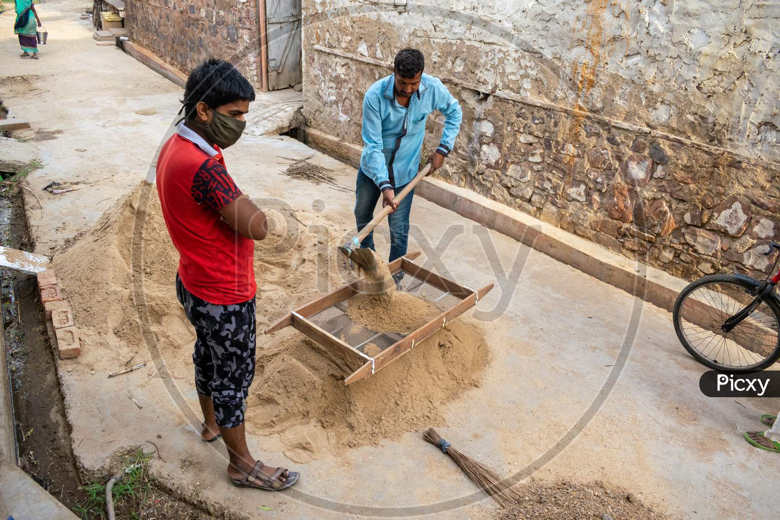 A man and a boy put bajri or gravel in a sieve to sieve it for construction
