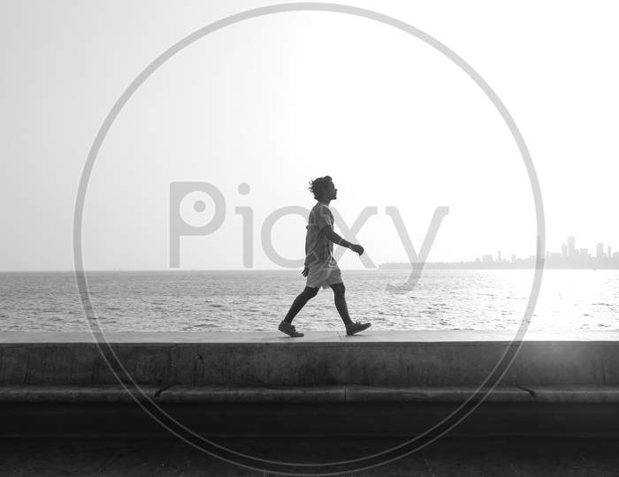A Young Boy In Shorts Walking On The Shore Of Ocean During Daytime