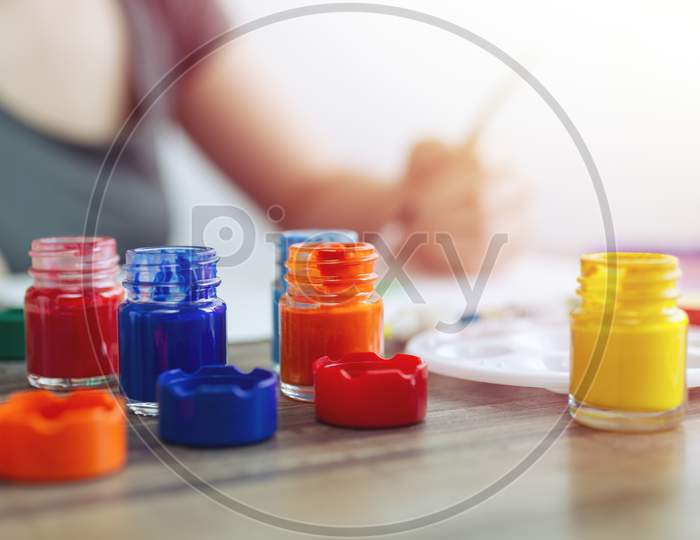 Close up of red, blue, yellow watercolor paint bottles set on wooden workplace. Art class or studio concept