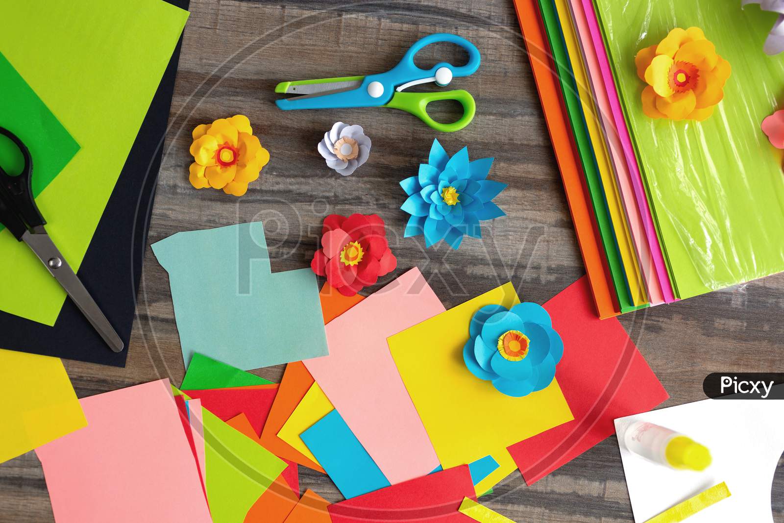 Flat lay of colorful  color paper flowers and scissors on wooden desk. Art studio workplace concept