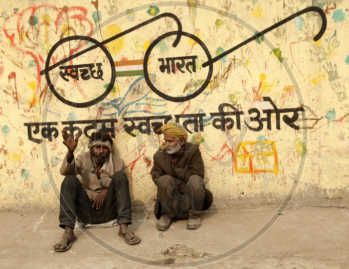 People sat alongside a wall with Swachh Bharath written on it