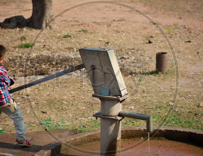 TIKAMGARH, MADHYA PRADESH, INDIA - NOVEMBER 20, 2019: Unidentified indian village little boy pumping hand water pump.