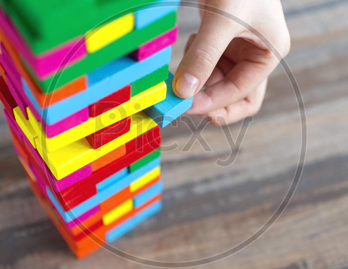 Close up of a hand pulling a colorful  jenga block from a big pile. Fun board games concept