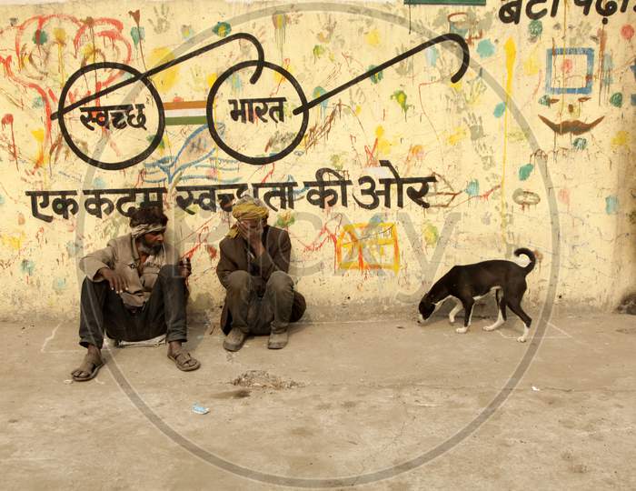 A couple of Men's sat alongside a wall with Swachh Bharath Written on it