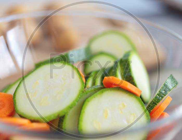 Close up of green zucchini cucumber and carrot slices in a bowl. Healthy food preparation concept