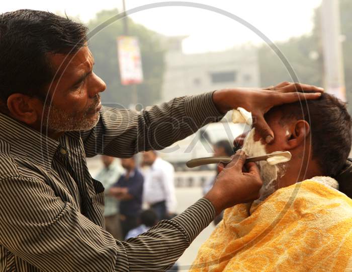 An Indian street barber giving his client a shave in a street