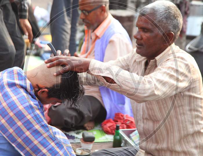 An Indian street barber giving his client a haircut in a street