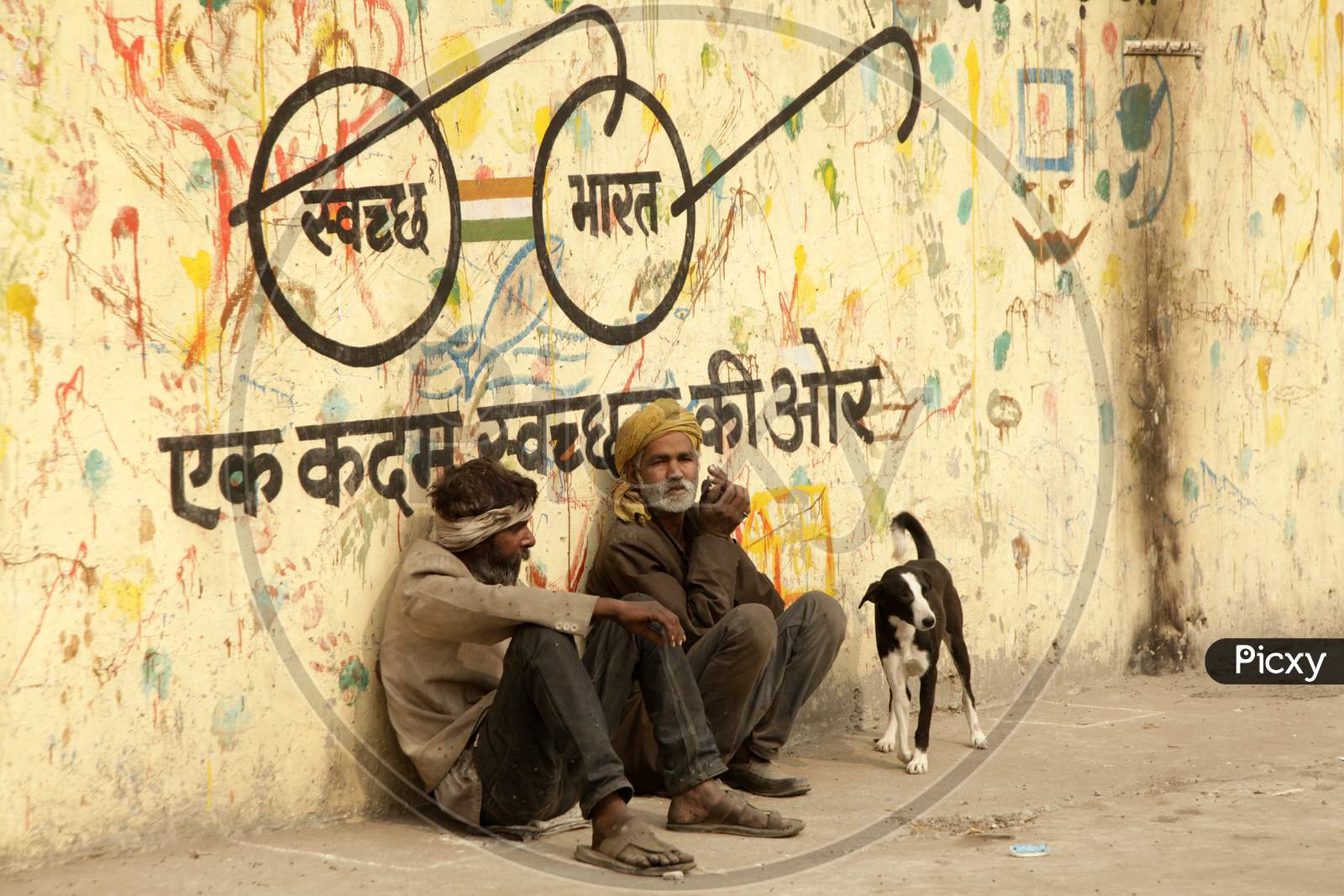 A couple of Men's sat alongside a wall with Swachh Bharath Written on it