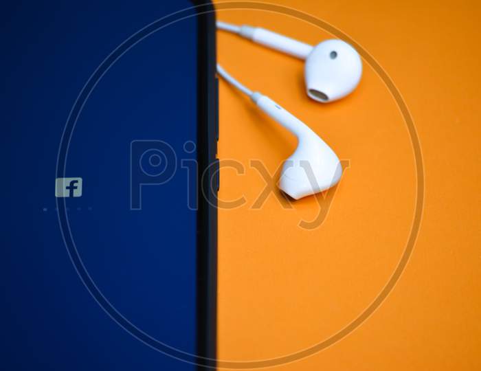 TIKAMGARH, MADHYA PRADESH, INDIA - DECEMBER 17, 2019: Facebook application loading on mobile phone screen with earphones. Facebook is largest and most popular social networking site in the world