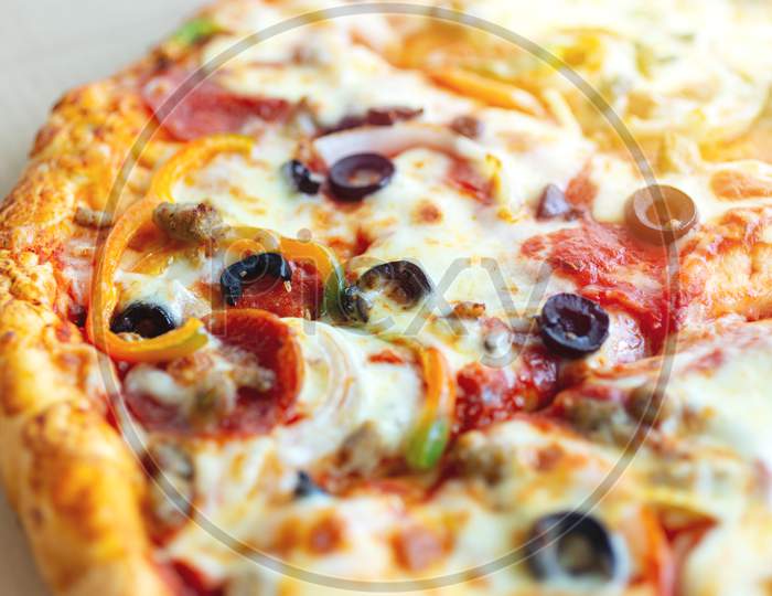 Close up texture of large cheesy pizza with olives, bell paper and salami, background macro