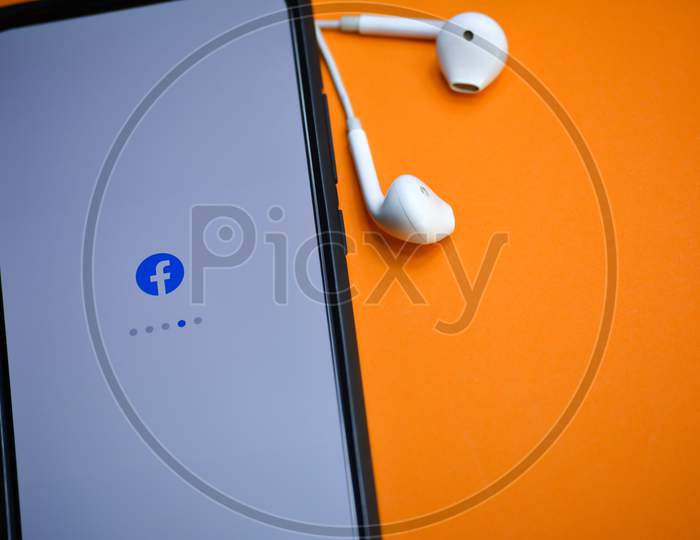 TIKAMGARH, MADHYA PRADESH, INDIA - DECEMBER 17, 2019: Facebook application loading on mobile phone screen with earphones. Facebook is largest and most popular social networking site in the world