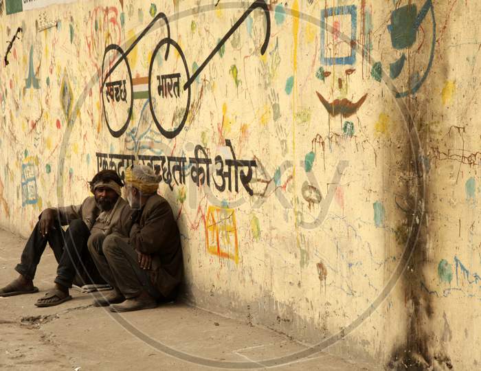 A couple of people sat alongside a Wall with Swachh Bharath written on it