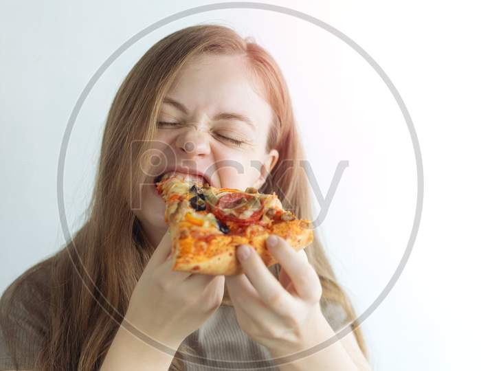 Young caucasian woman girl hungrily biting eating a slice of pizza with a funny face