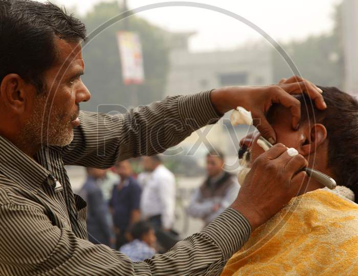 An Indian street barber giving his client a shave in a street