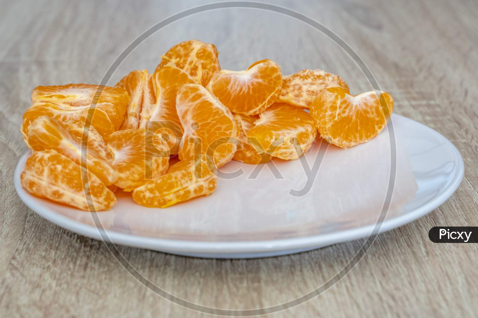 Close Up Of Pealed Mandarin Peaces On White Plate, Wooden Desk Surface