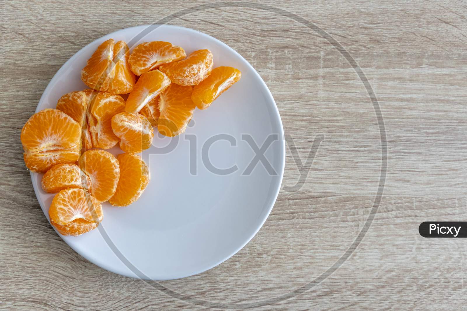 Top Down View Of Pealed Mandarin Peaces On White Plate, Wooden Desk Surface