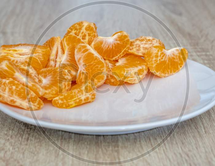 Close Up Of Pealed Mandarin Peaces On White Plate, Wooden Desk Surface