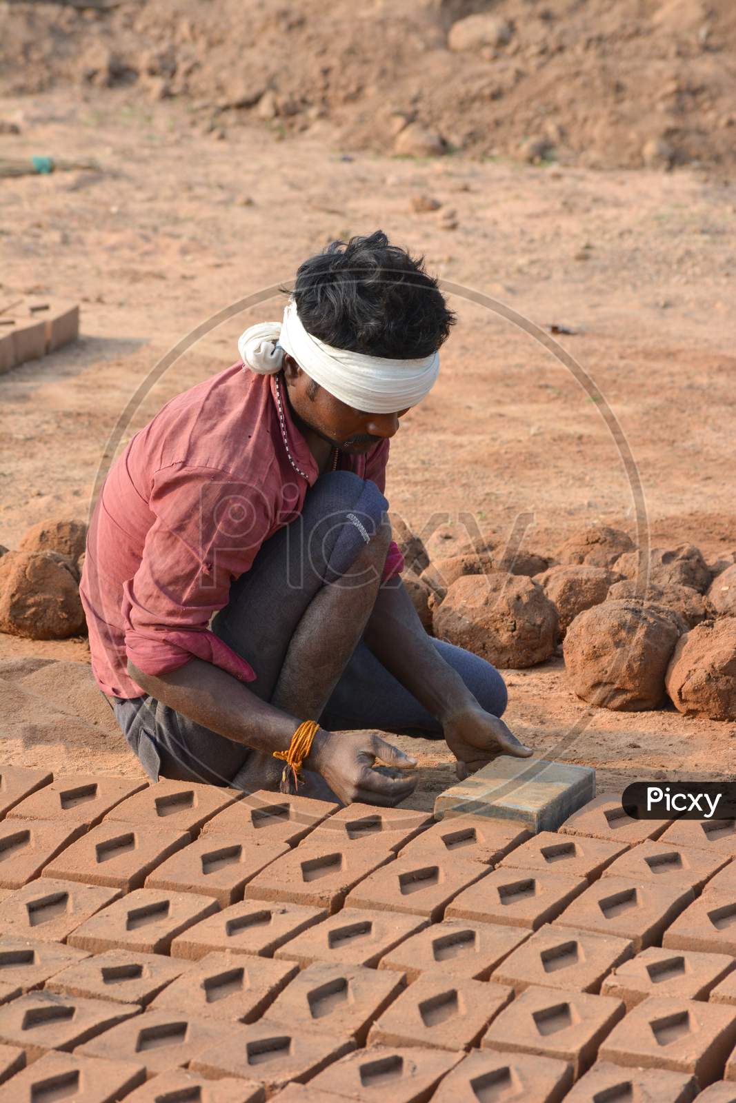TIKAMGARH, MADHYA PRADESH, INDIA - FEBRUARY 07, 2020: Unidentified Indian man making house bricks by hand using a mold and wet clay.