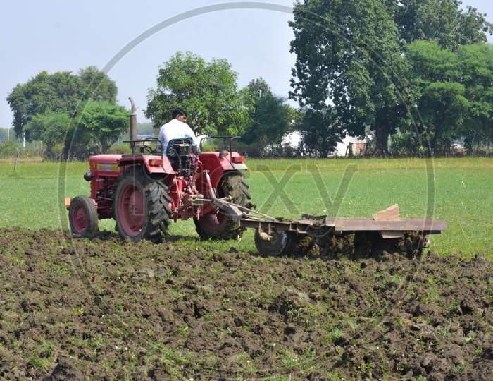 TIKAMGARH, MADHYA PRADESH, INDIA - NOVEMBER 10, 2019: Indian farmer with tractor preparing land for sowing with harrow.